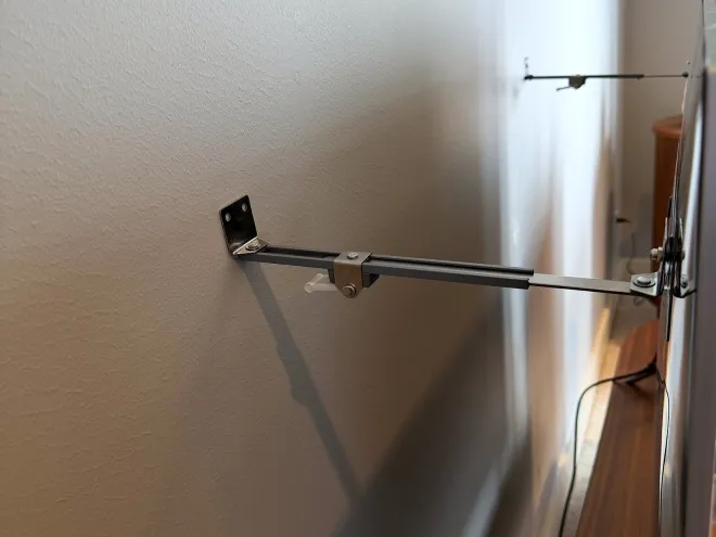 One rigid anti-tip brace: a metal arm screwed to the wall and locked to the back of the TV.